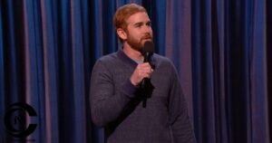 Andrew Santino performing stand-up comedy on stage holding a microphone