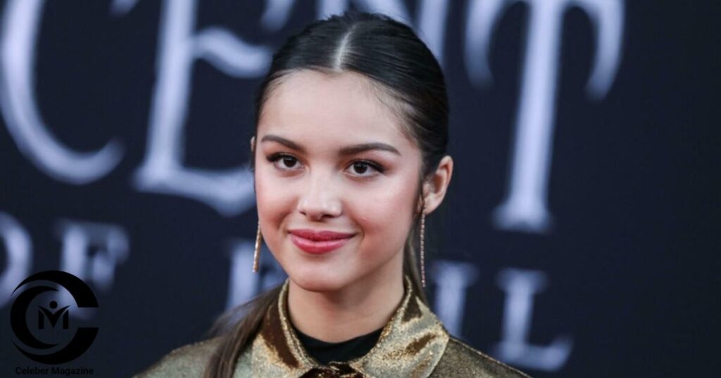Olivia Rodrigo posing on the red carpet in a gold outfit with a sleek hairstyle, attending a public event.