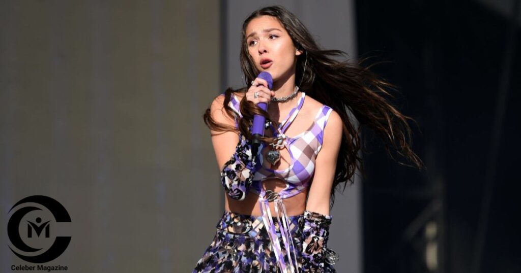 Olivia Rodrigo performing live on stage in a patterned outfit, holding a purple microphone.