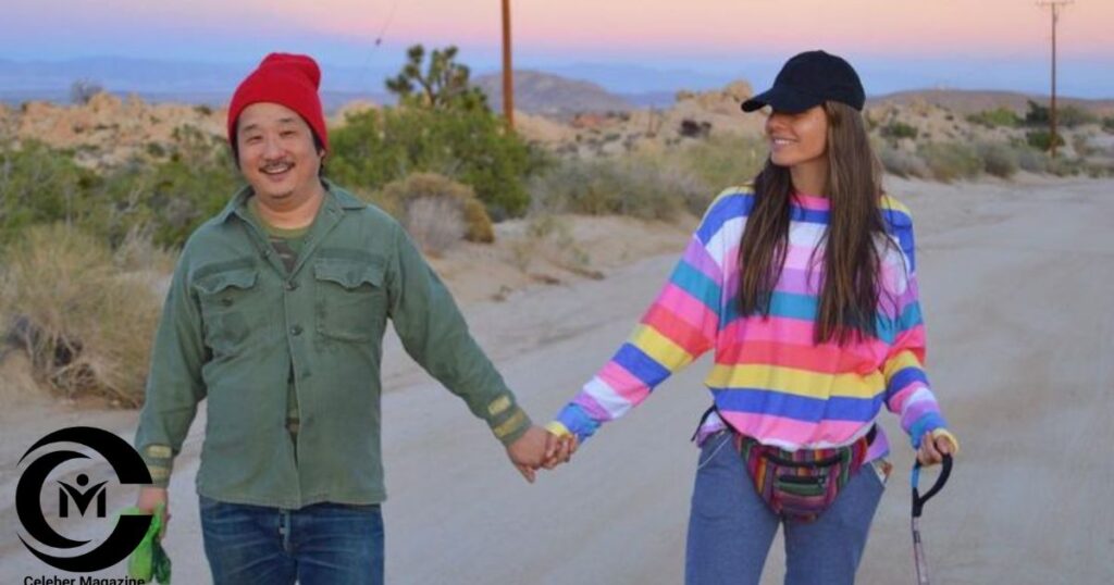 Bobby Lee holding hands with a woman in a colorful outfit while walking outdoors at sunset.